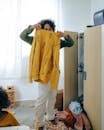 Unrecognizable African American teen girl in casual wear holding yellow sweater while sorting clothes in wardrobe in room