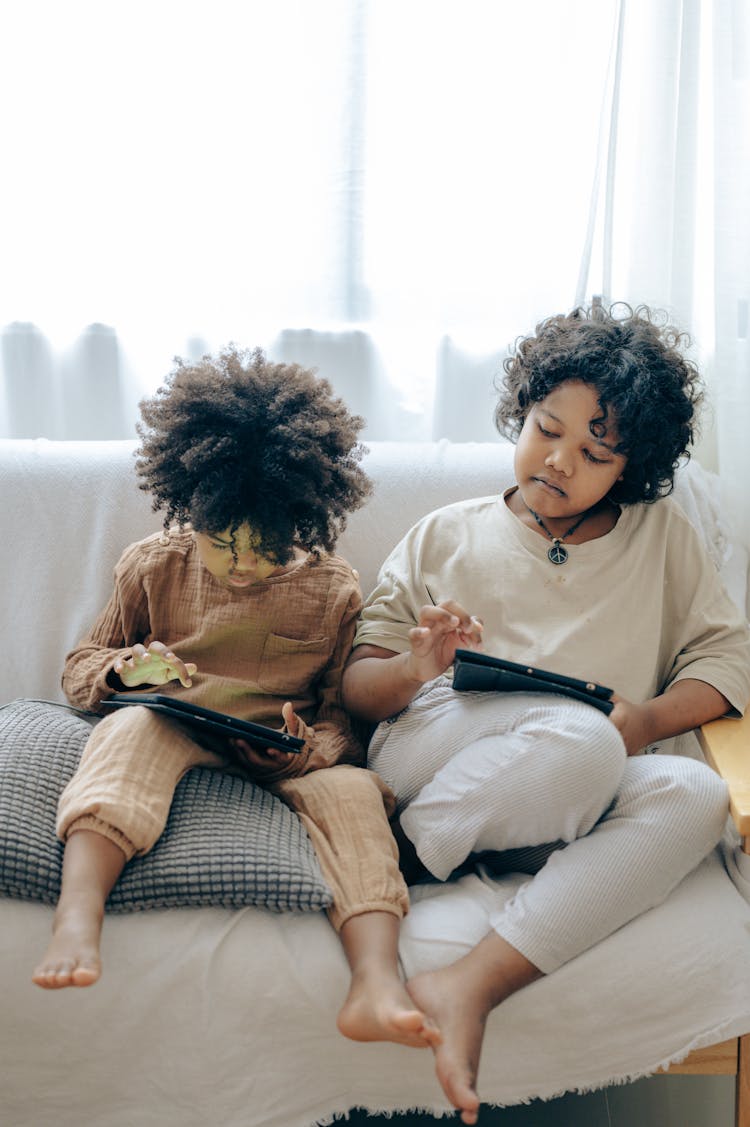 Little Black Kids Using Tablets On Couch At Home