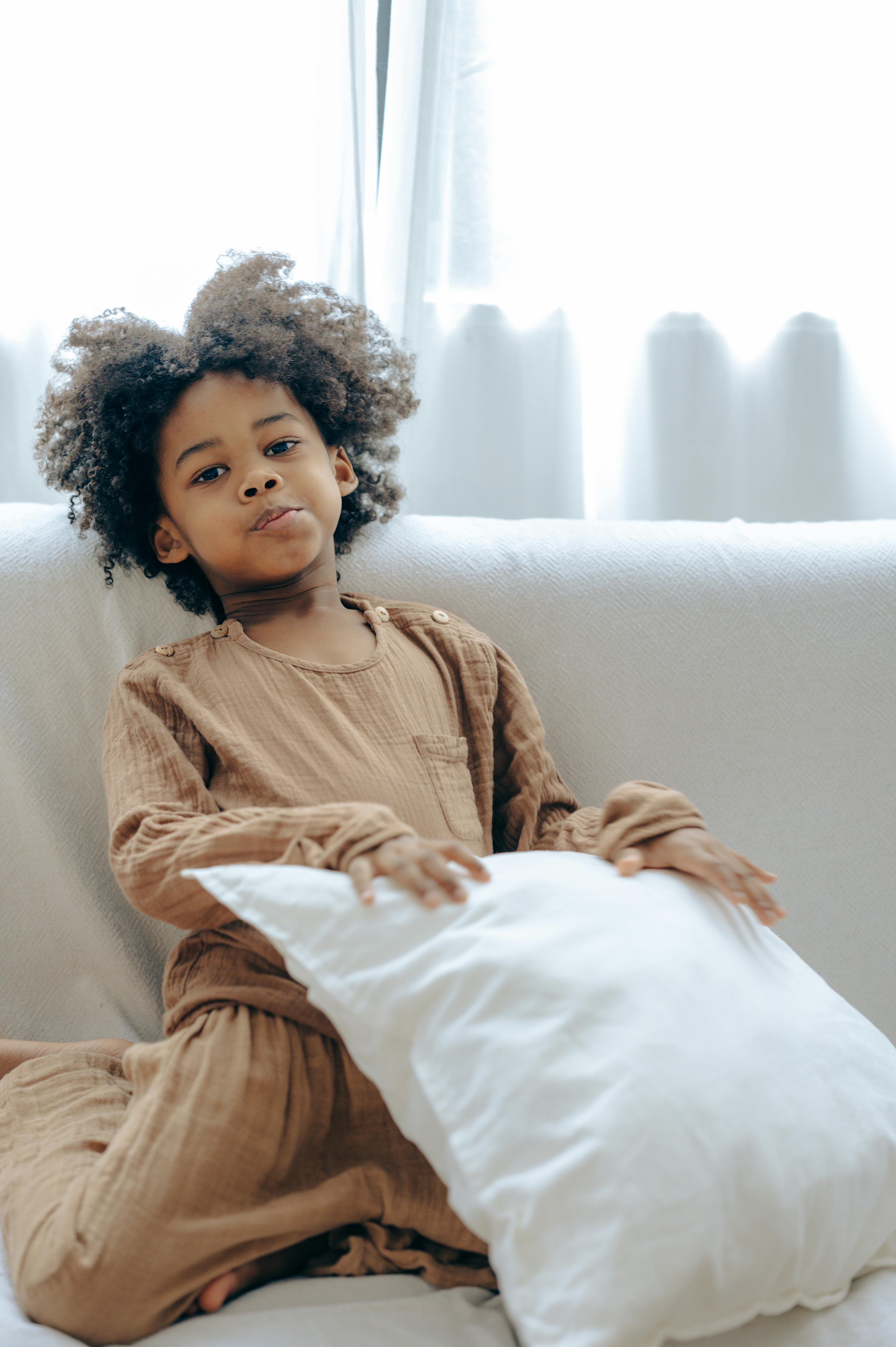 mischievous little black girl resting on sofa with pillow