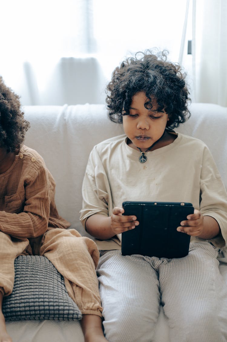 Concentrated Black Kid Using Tablet On Couch