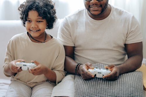 Crop unrecognizable young African American man playing console game with cute little daughter using controllers