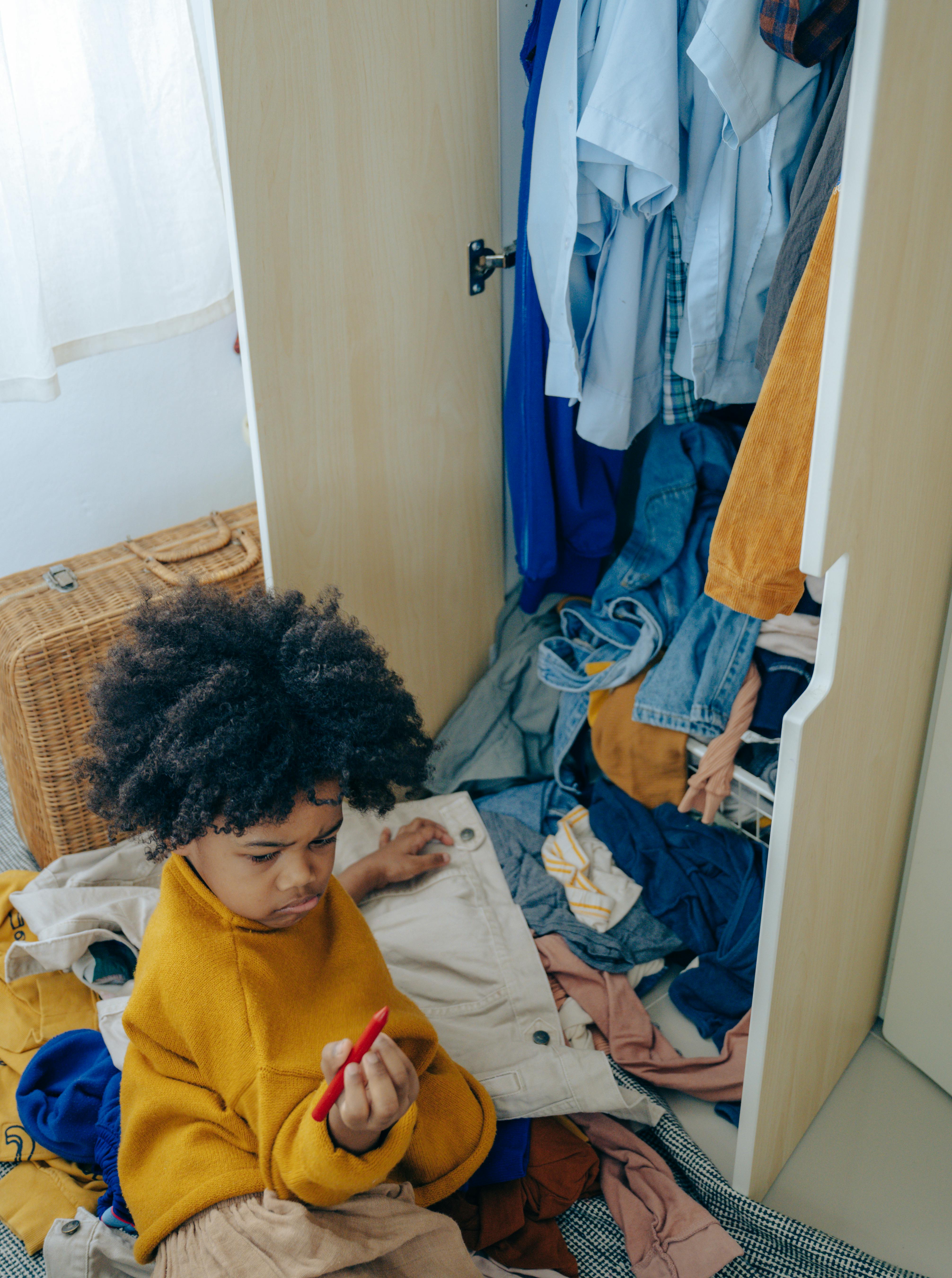 curious little black kid making mess of clothes in wardrobe