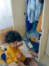 Curious little black kid making mess of clothes in wardrobe