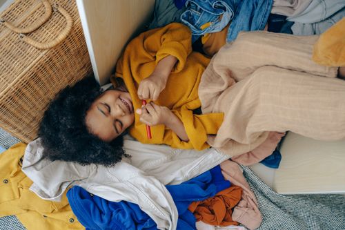 Free Top view of funny cute little African American girl lying on pile of scattered clothes and drawing on hand with marker Stock Photo