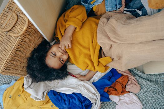 Cute little African American child lying on stack of clothes