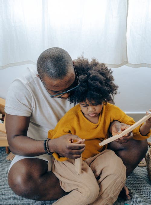 Free High angle of young black man taking care of little daughter while playing together sitting on floor Stock Photo