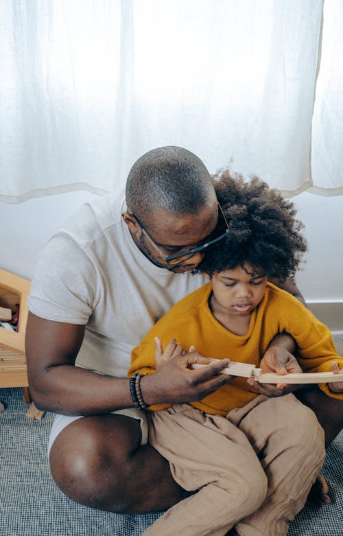 Focused black father and daughter playing with wooden puzzle sitting on floor