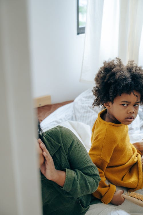 Offended little girl sitting on bed with sibling