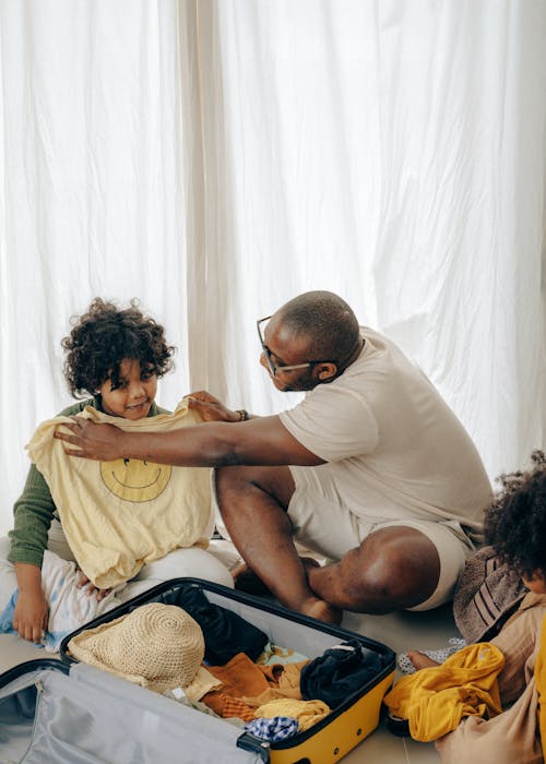 Black dad and kid sorting clothes while packing suitcase