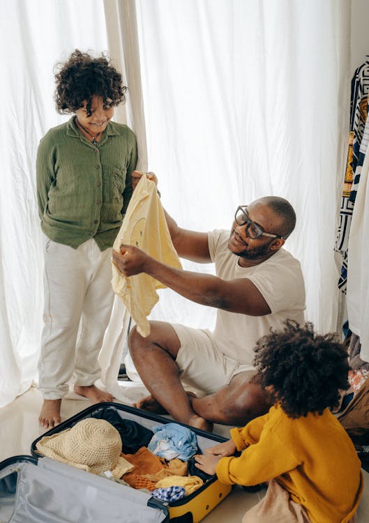 Free Happy African American male in glasses and casual clothes with children packing suitcase Stock Photo