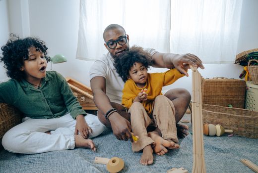 African American man in casual wear and eyewear sitting on floor and playing with kids with curly hair