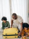 African American male in eyeglasses sitting with sad children with curly hair on floor and packing suitcase