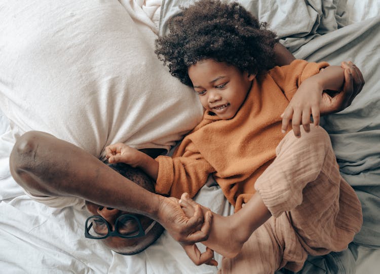 Black Father And Kid Lying On Bed