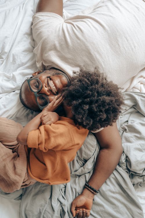 Free Top view of delighted African American father in eyewear and kid with curly hair smiling and lying on bed together Stock Photo