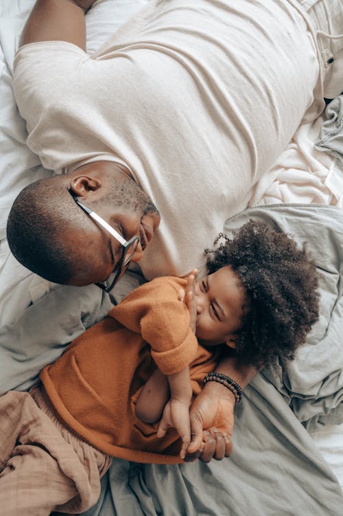 Free Top view of smiling black father in glasses and kid with curly hair lying on bed and looking at each other Stock Photo