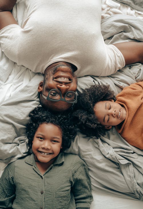 Happy children lying on bed with father