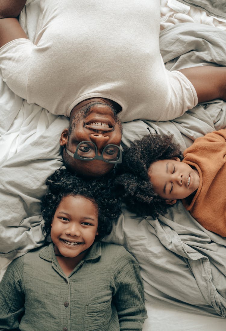 Happy Children Lying On Bed With Father