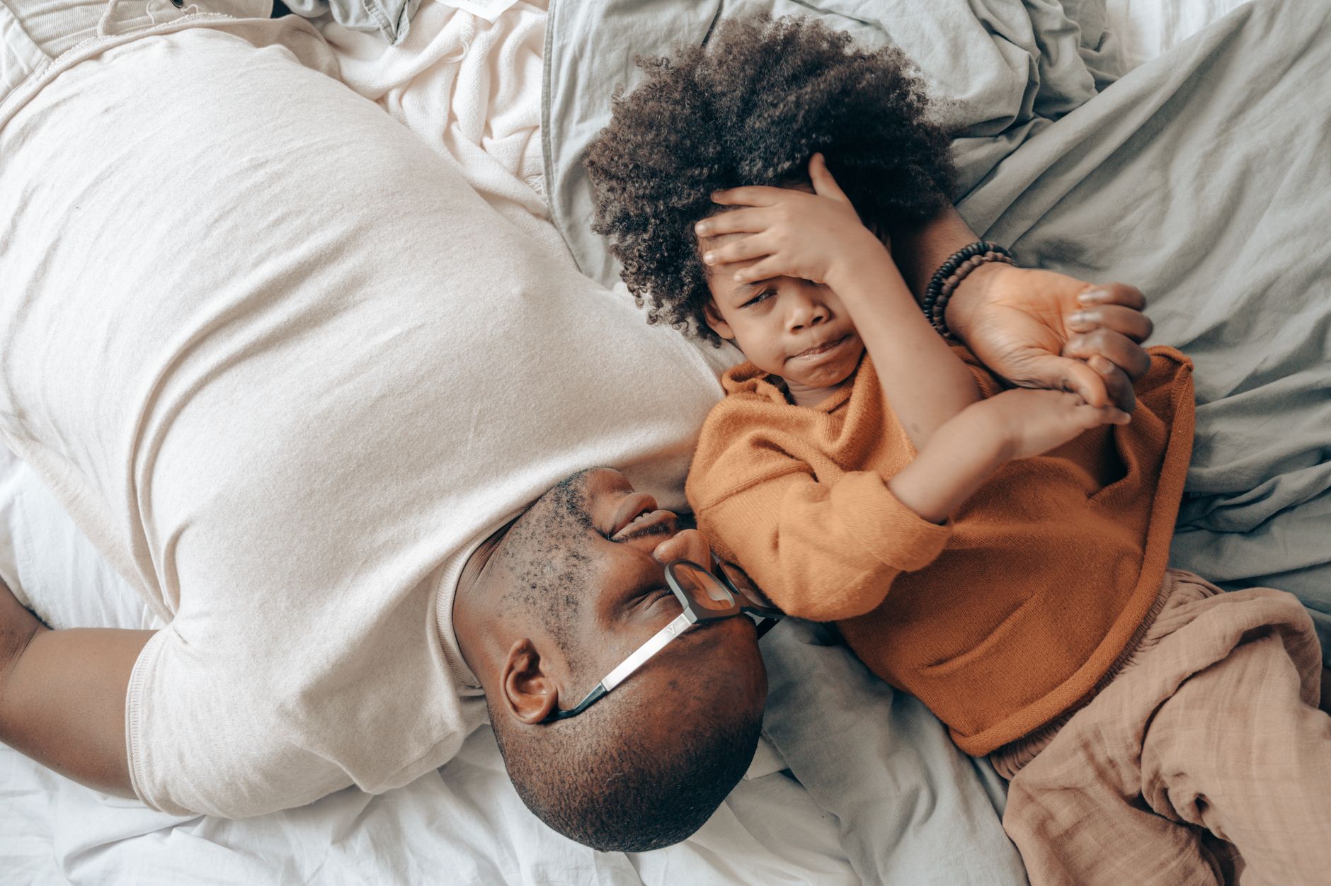 From above of African American man and child lying face to face and hugging while talking with each other in comfortable bedroom on weekend day