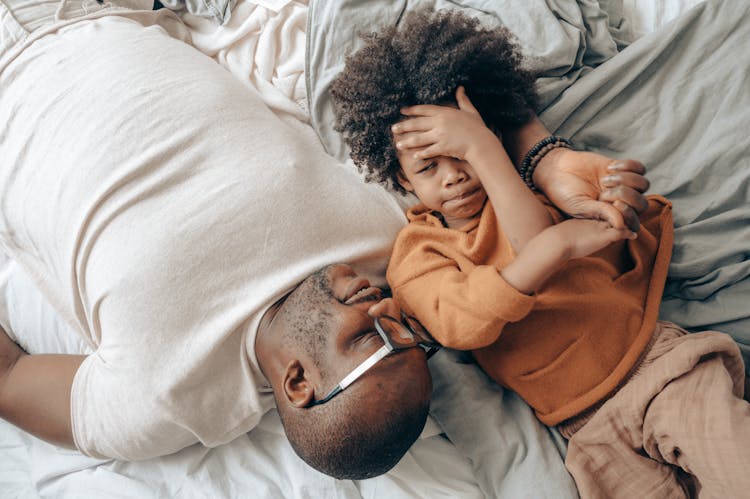 Ethnic Dad And Kid Resting Together On Bed