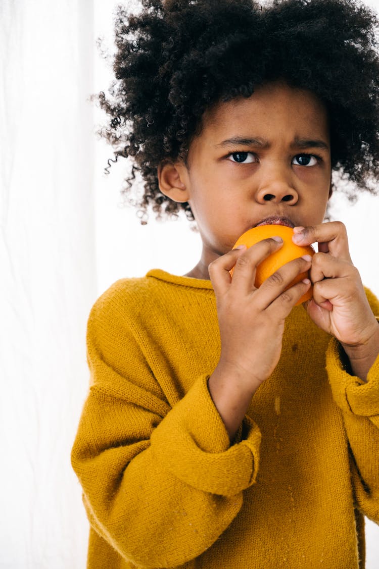 Serious Ethnic Child Tasting Fresh Fruit On White Background