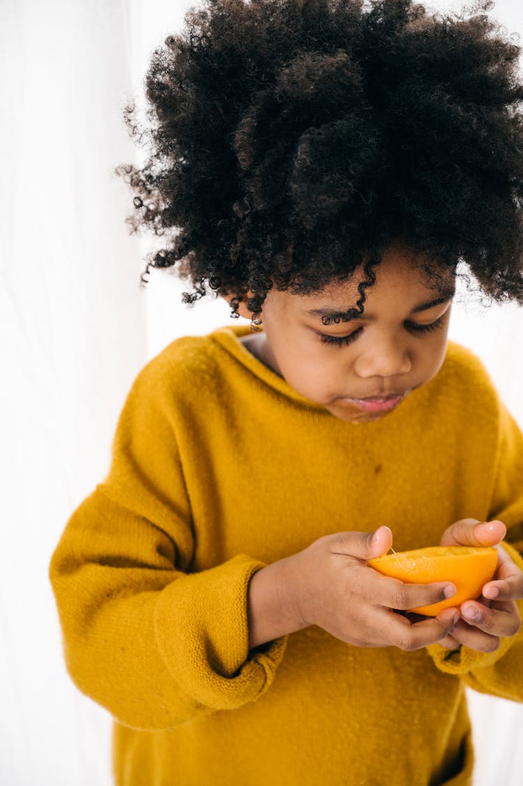 Amazed Ethnic Child With Orange On White Background