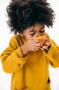 Adorable African American kid with curly hair in casual clothes eating orange with closed eyes on white background