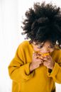 Cute African American curly kid with dark hair in vivid hoodie eating heartily fresh citrus while standing on white background