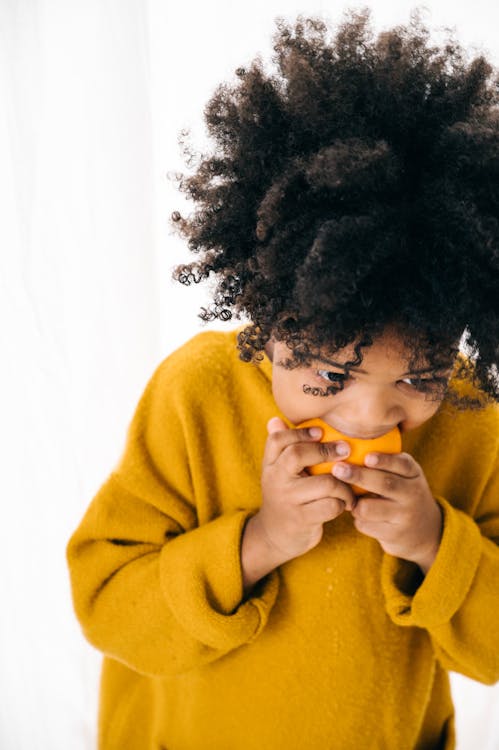 Hungry ethnic child eating ripe orange in studio