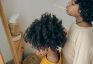 From above side view of ethnic children in casual outfit brushing teeth together in front of mirror in cozy bathroom