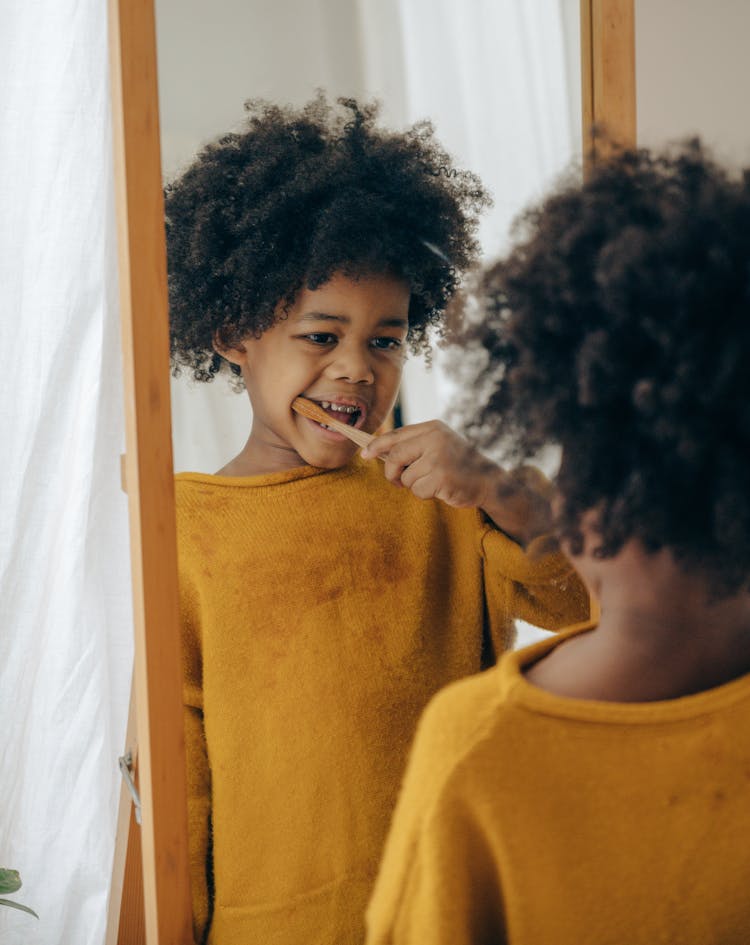 Black Child Brushing Teeth In Front Of Mirror