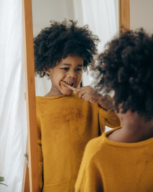 Free Ethnic kid in bright casual clothes carefully cleaning teeth with toothbrush in front of mirror in bathroom Stock Photo