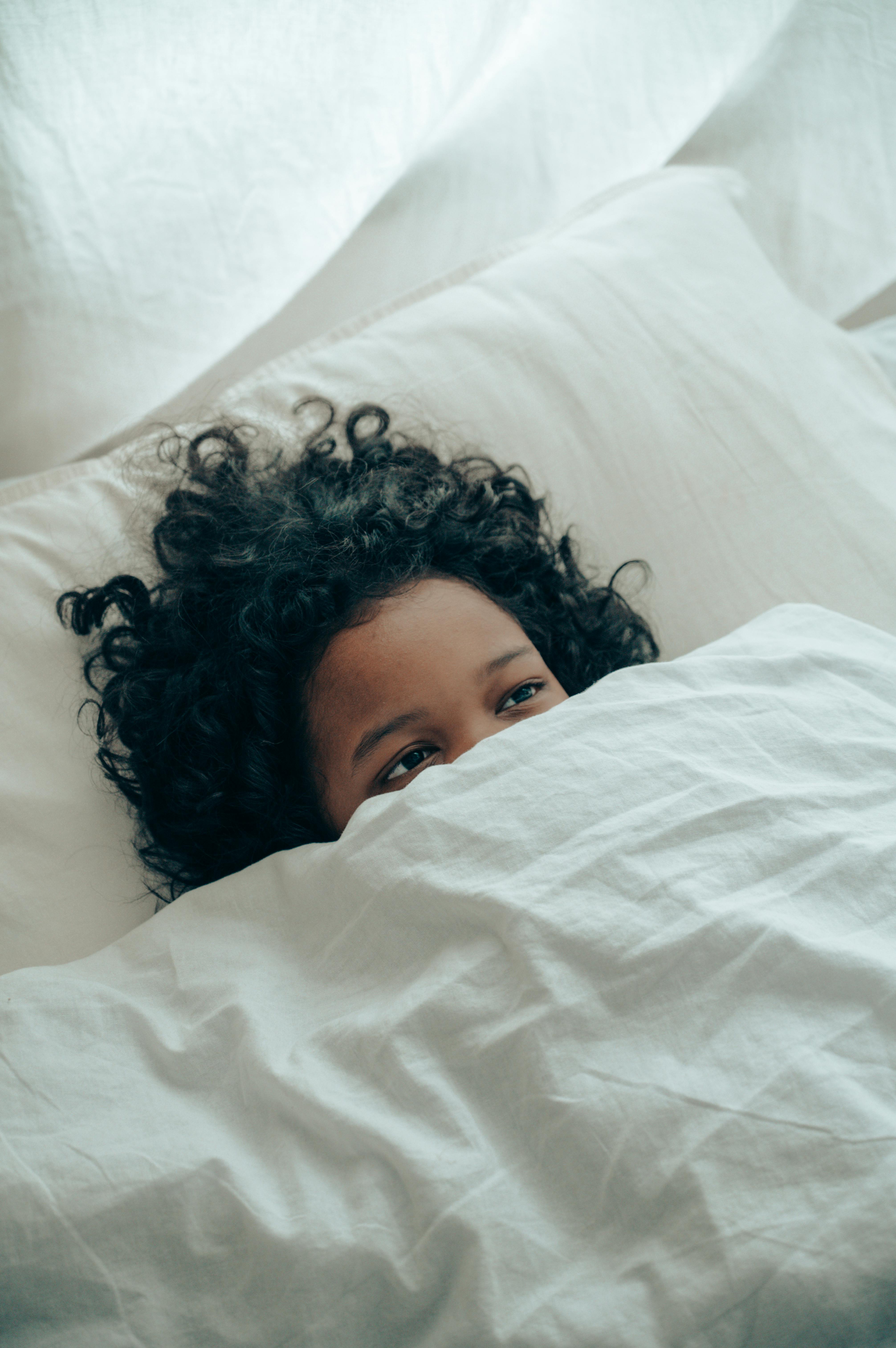 ethnic child covering half of face with blanket lying in bed