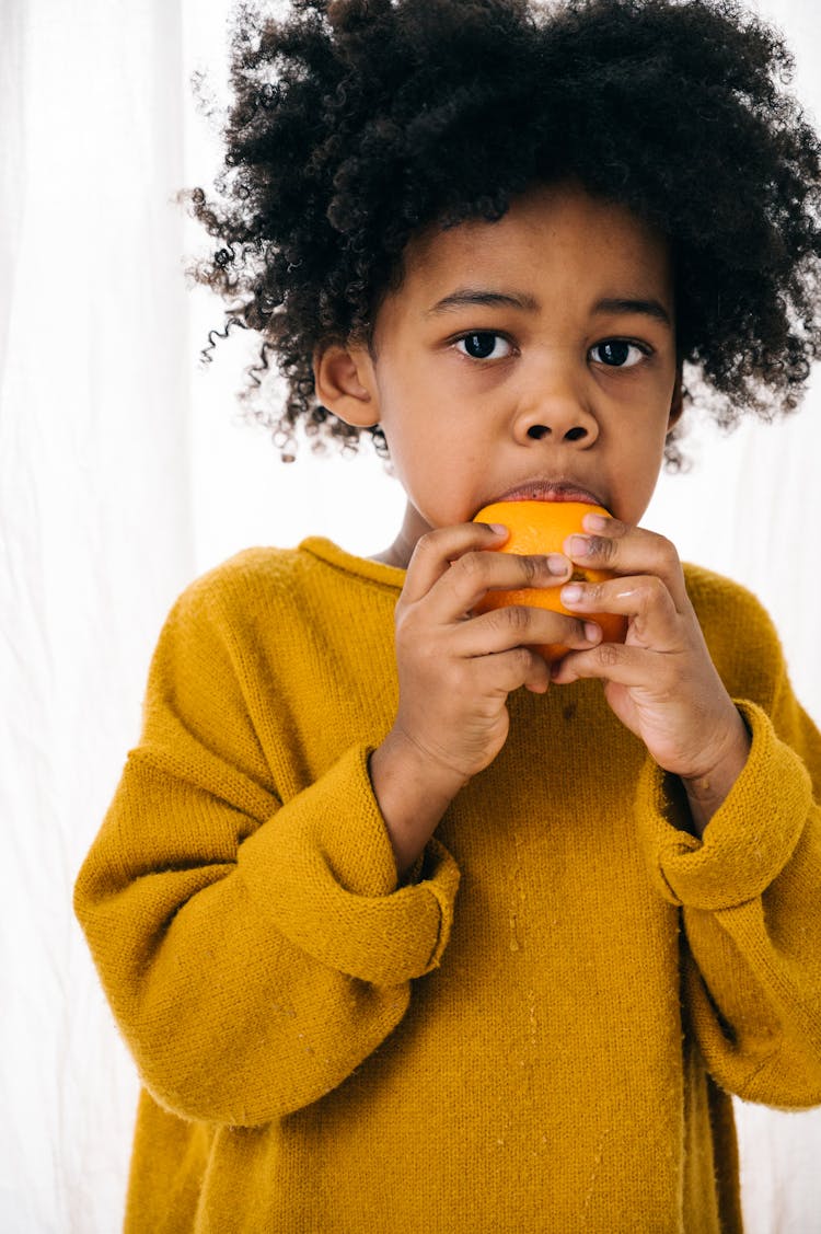 African American Kid Eating Orange At Home