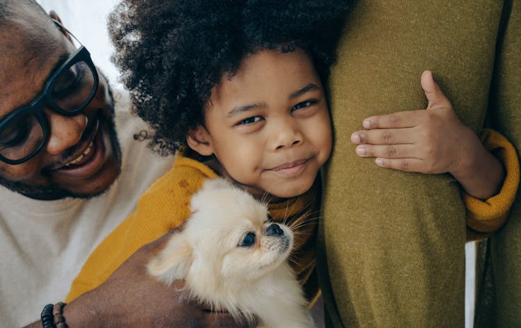 African American Kid Hugging Dog And Leg Of Parent