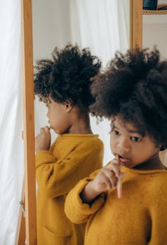 A young child brushes teeth in front of a mirror, enjoying morning hygiene routine.