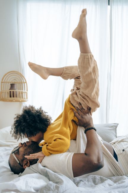A joyful moment of a father and child playing on bed indoors, capturing family love.