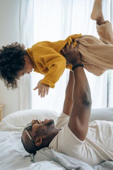 A father and child share a joyful moment playing indoors on a sunny day.