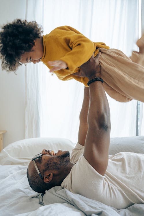 Free Delighted father lying on bed and lifting up happy son Stock Photo