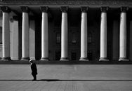 Black and white side view of anonymous senior man on tiled pavement against aged building with columns in city