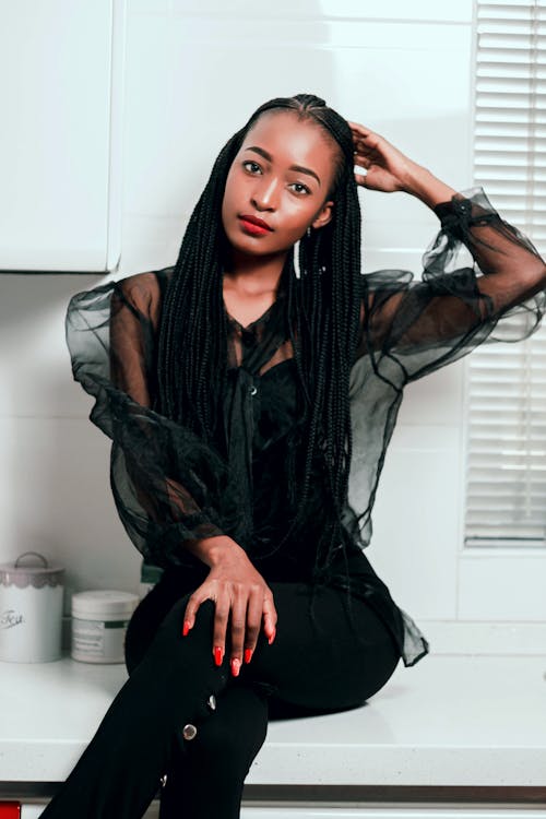 Charming young African American female in stylish black outfit sitting on white windowsill