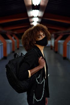 African American man with backpack wearing a mask in a dimly lit tunnel.