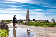 Woman in Black Jacket Walking on Brown Sand Near Body of Water