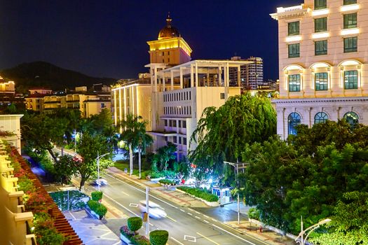 夜晚的城市街景充满活力，建筑物明亮，绿化郁郁葱葱