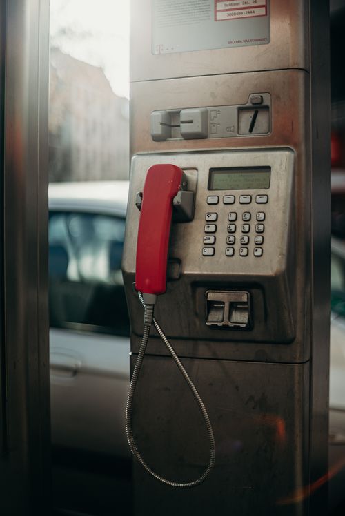 Free Old-fashioned payphone with a red handset in a city street scene, showcasing urban technology. Stock Photo
