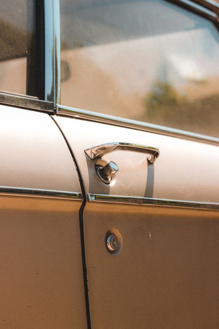 Chrome knob on door of old fashioned automobile parked on street in sunny day