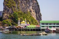 Picturesque scenery of Ko Panyi floating village with traditional colorful houses and mosque with golden domes located near huge rocky cliff in Thailand