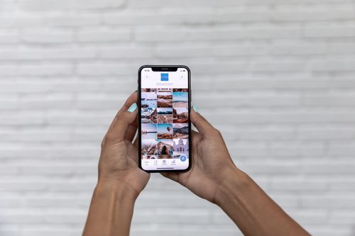 Free Close-up of woman holding a smartphone displaying a social media app against a brick wall. Stock Photo