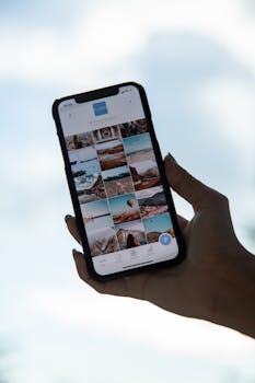 A smartphone in hand showing a gallery of travel photos against a clear sky.