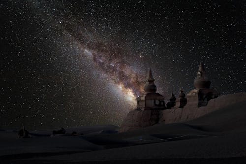 Spectacular scenery of frozen snowy historic architecture on vast winter valley beneath dark night sky with numerous bright glowing stars