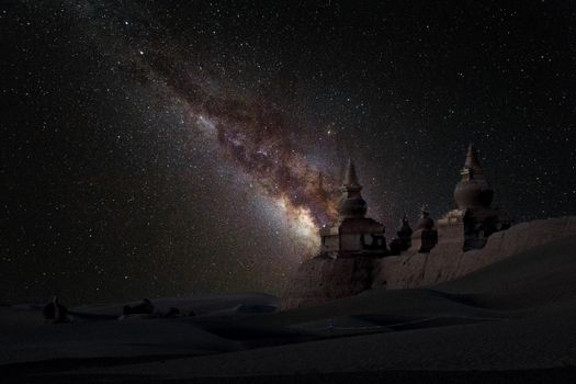 在漆黑的夜空下，广阔的冬季山谷中，白雪皑皑的历史建筑呈现出壮丽景色，周围有无数明亮的星星闪耀